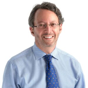 Dr. Rudderman Plastic Surgeon in a headshot with a blue shirt and darker blue tie wearing glasses