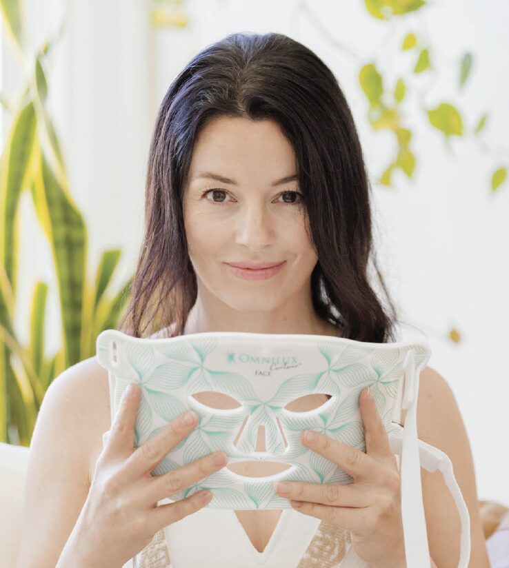 Female smiling and holding Omnilux Face mask